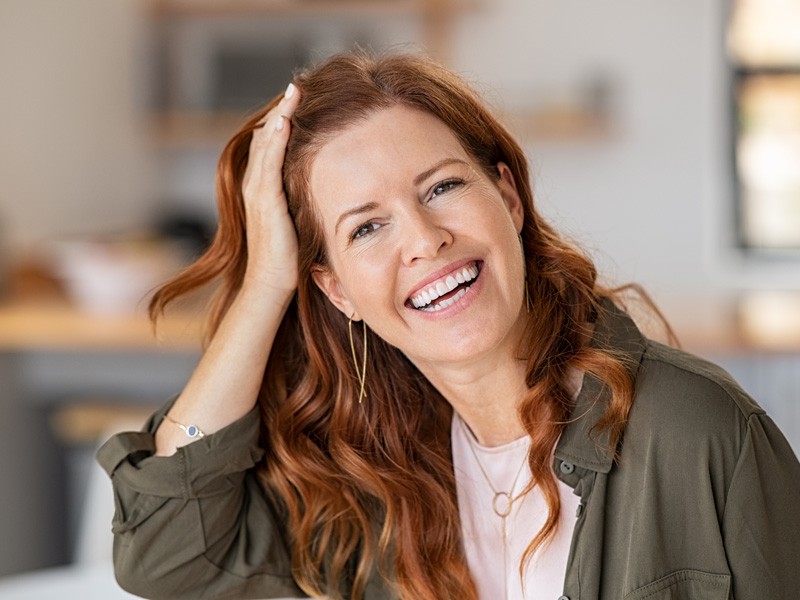 A red-haired woman smiles, gently touching her head after Plexr treatment in greater Edmonton